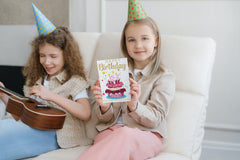 Birthday girl holding birthday card sitting next to her friend playing a mini guitar