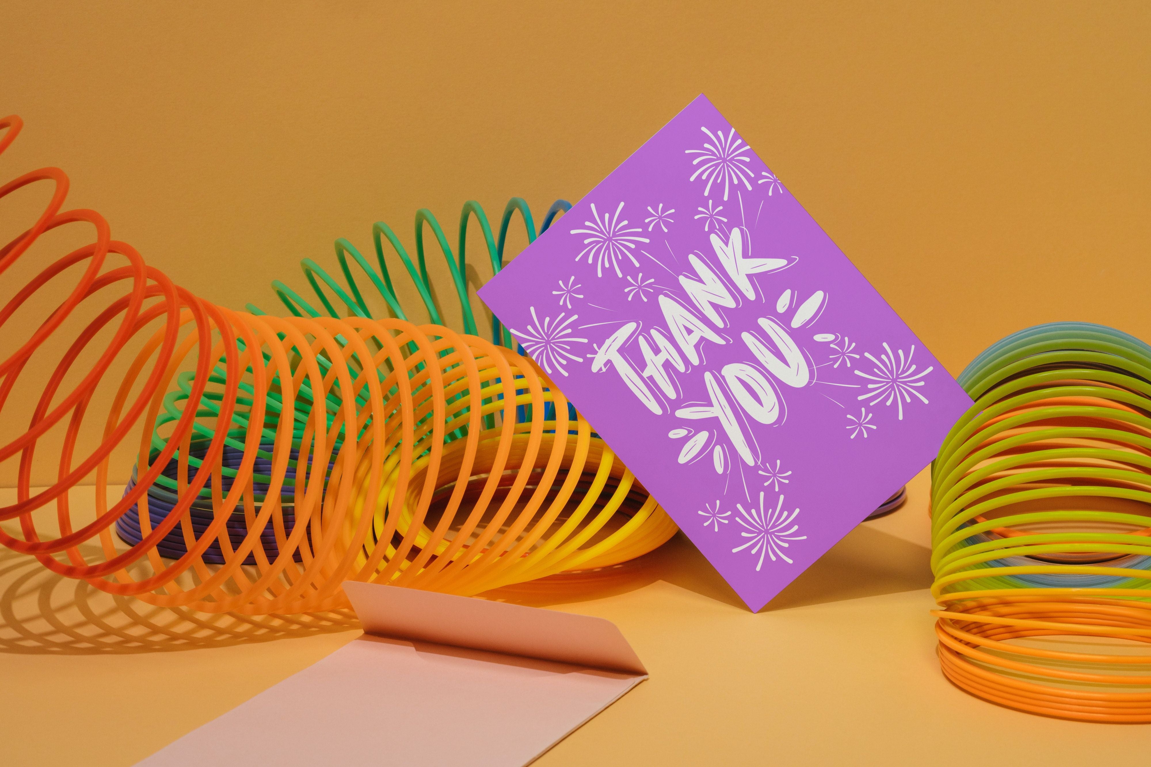 Purple card saying Thank you with fireworks leaning on rainbow colored slinky.