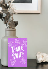 Purple card saying Thank you with fireworks standing against vase of flowers.