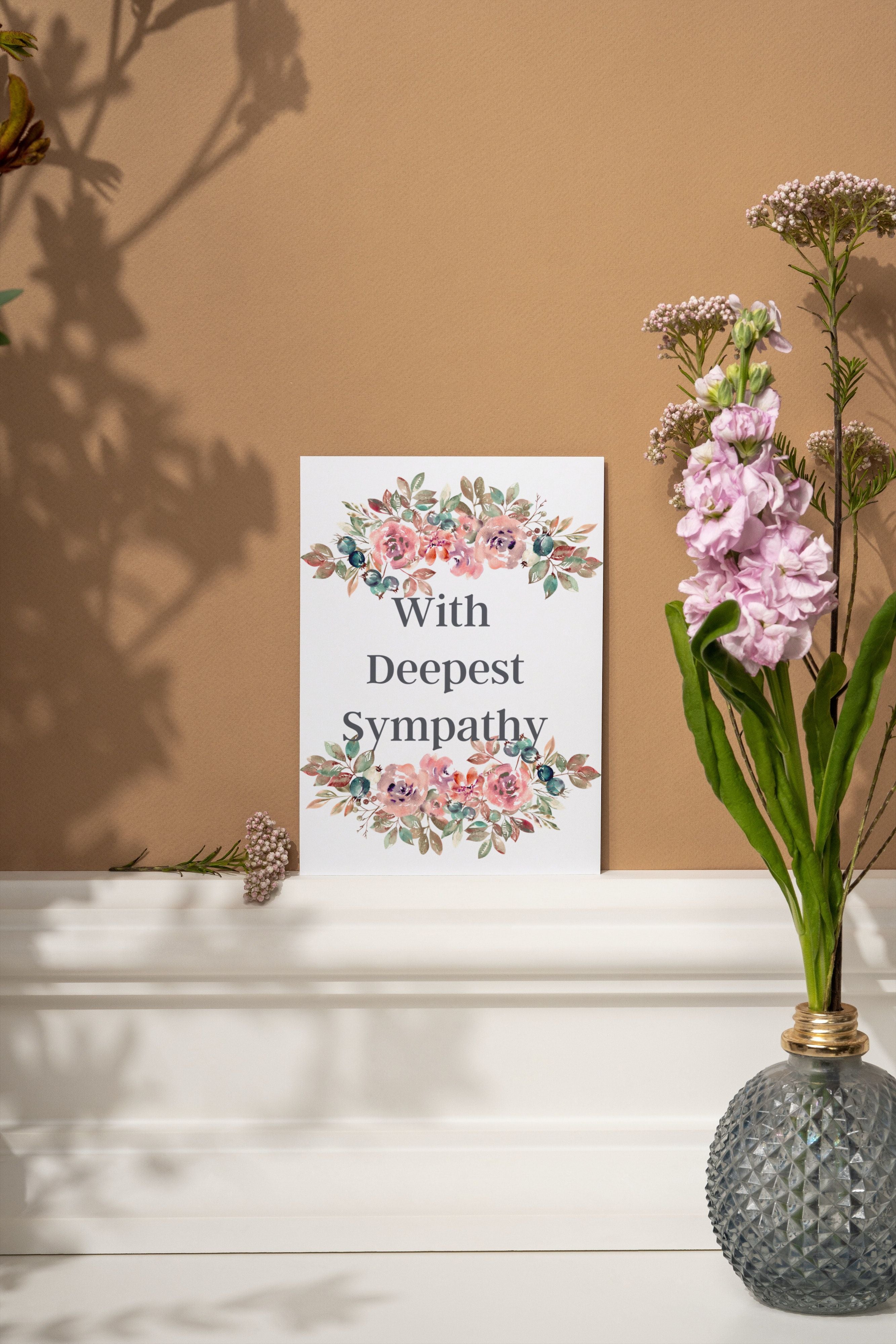 Floral card saying, With deepest sympathy standing against brown wall next to vase of flowers.